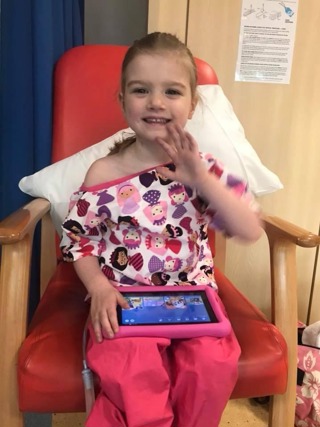 A little girl in hospital sat on a chair waving