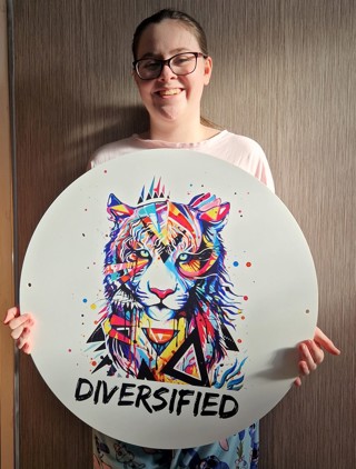 Kaydi holding the Diversified charity logo - a multicoloured tiger