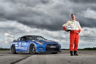 Mike Newman, Speed of Sight founder, standing with a race car in his racing outfit.