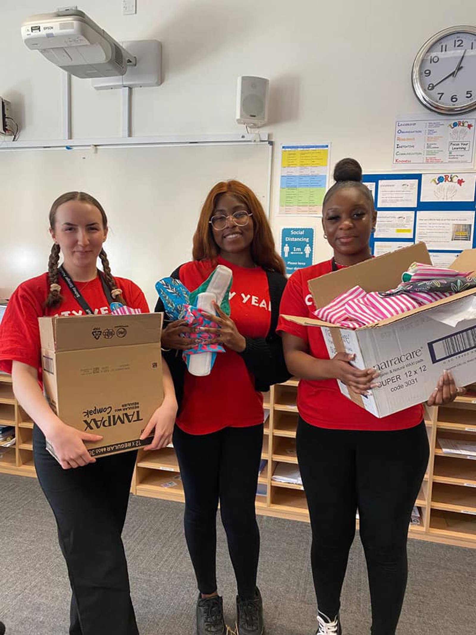 Three girls stood with boxes of period product donations.