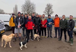 A group of men and three dogs, about to go on a walk in the countryside.