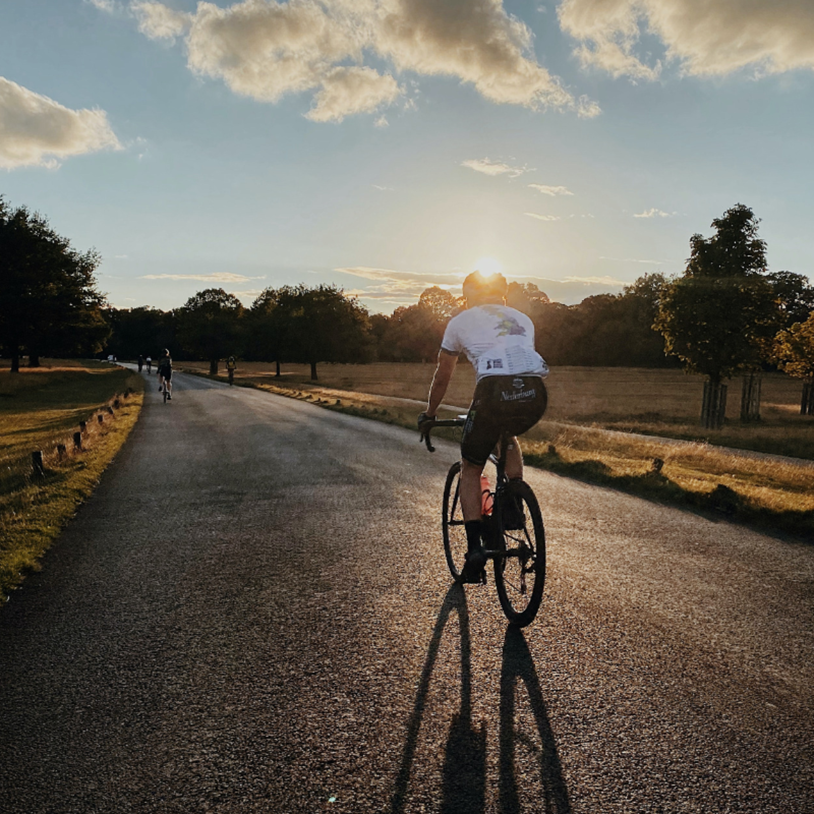 Man on a road bike cycling along road towards a sunset